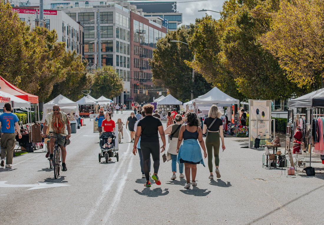 Walkers, a cyclist and a stroller filling a car-free Howell Mill Road, vendor tents lining both sides